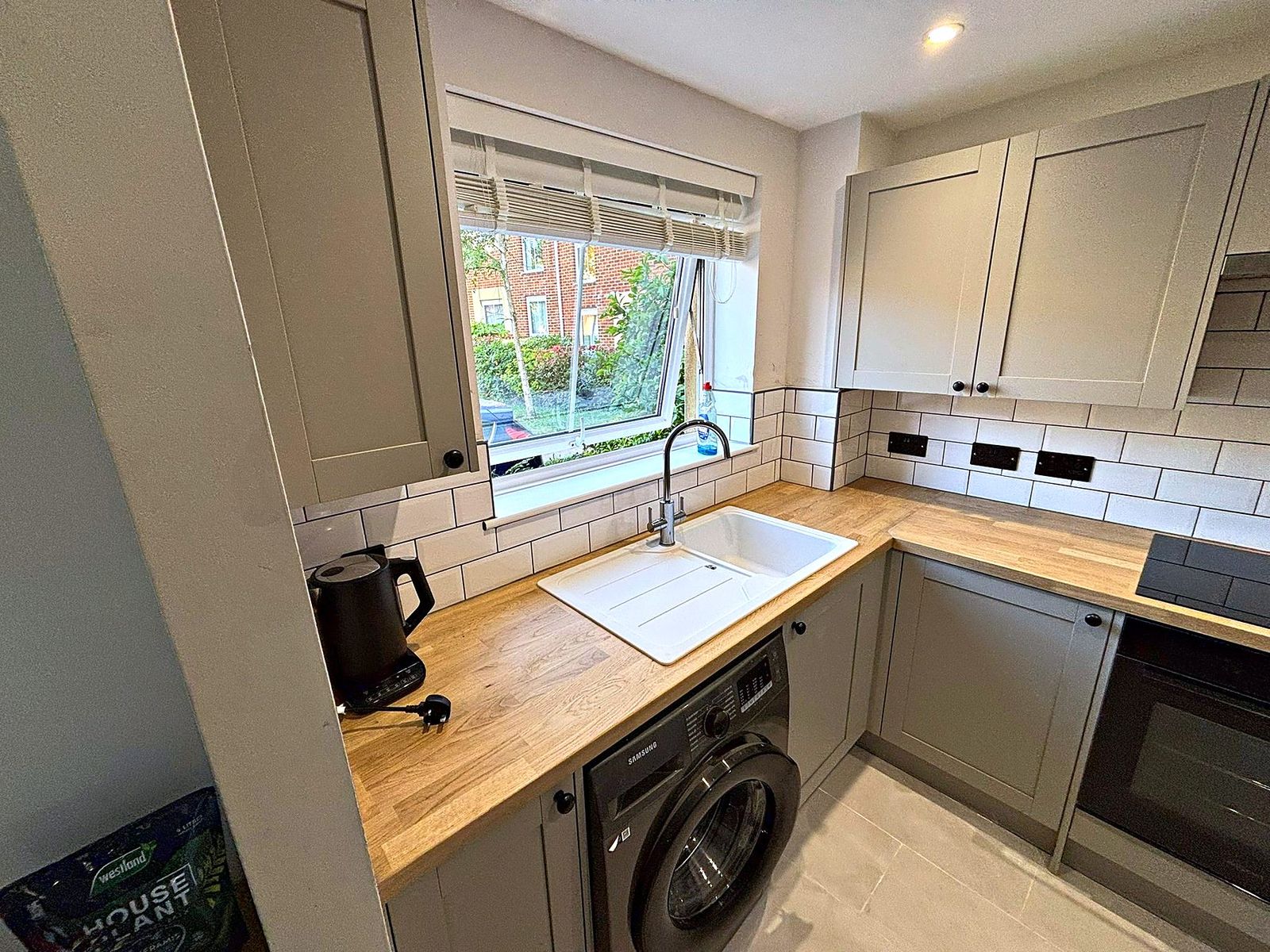 Sage shaker kitchen with ceramic sink beneath the window and oak worktops