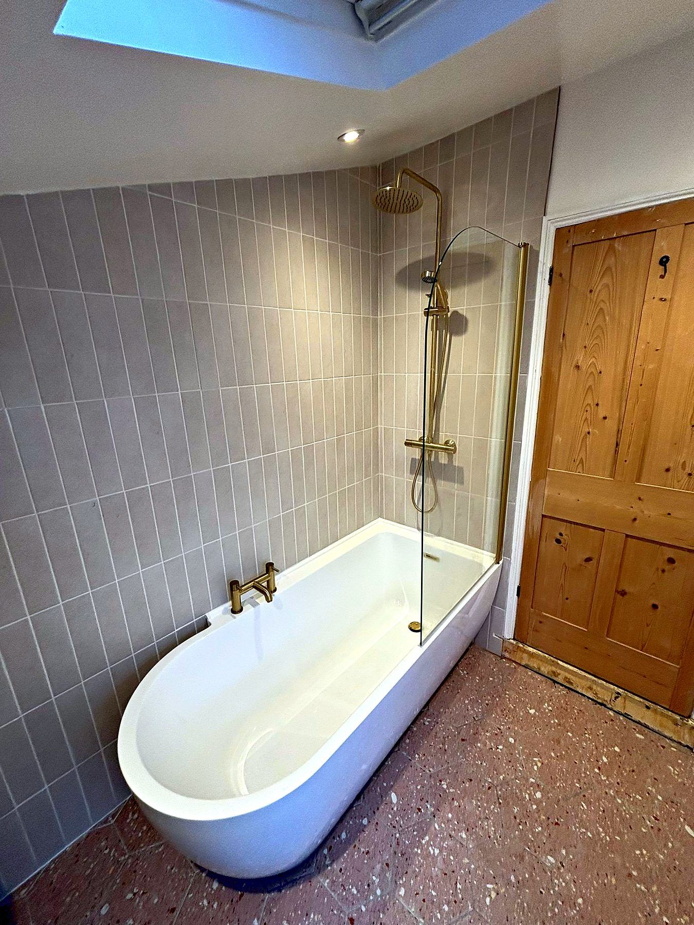 Double-ended bath with brushed brass shower, glass screen and a stripped pine door