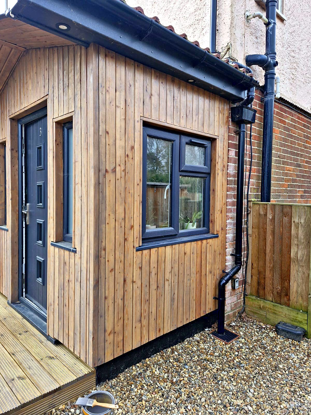 Timber-clad porch extension with anthracite door and window, built onto a red brick house