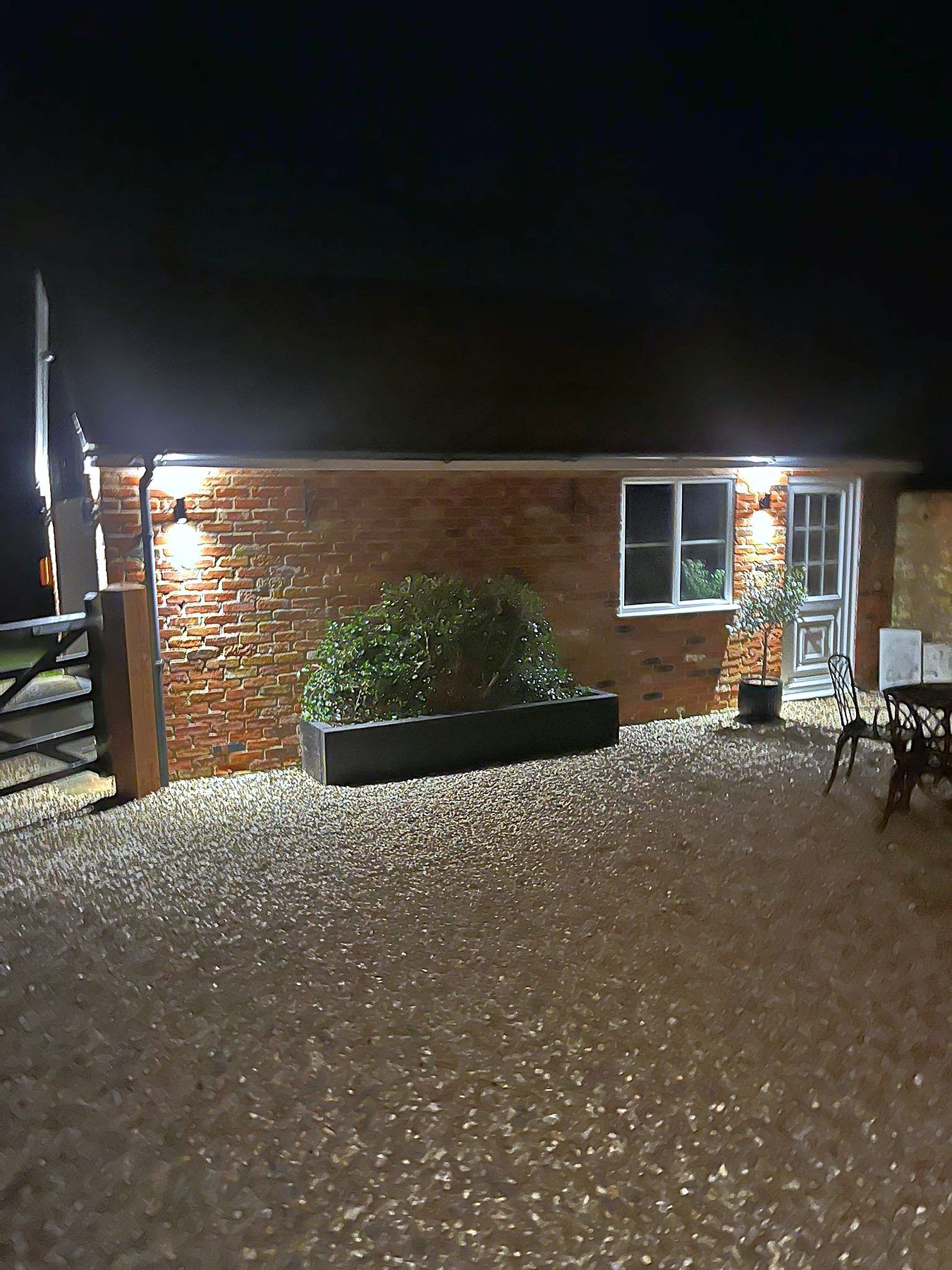 Brick bungalow and gravel courtyard lit at night by newly fitted exterior wall lights