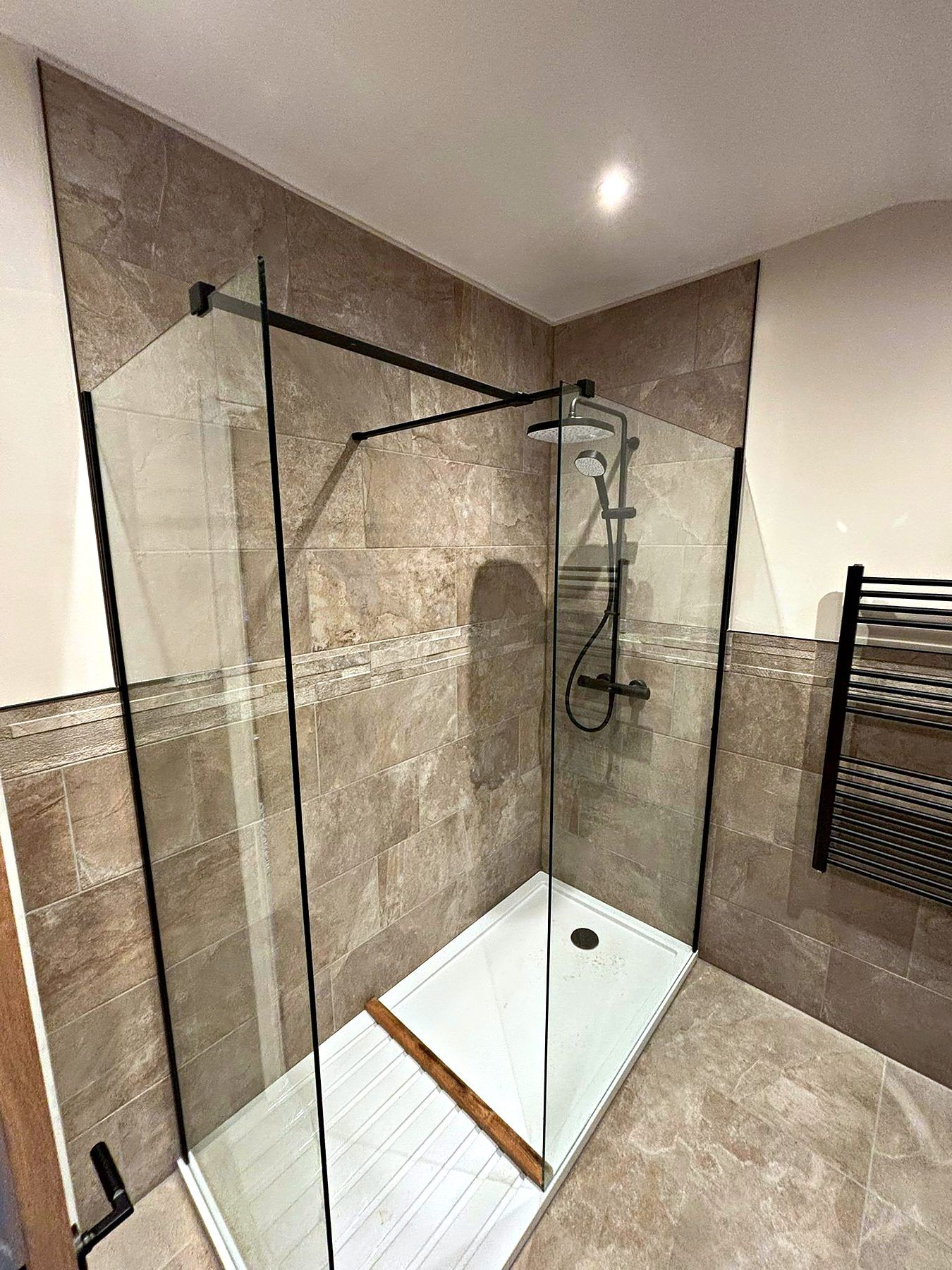 Walk-in shower with black framed glass screen, stone-effect tiling and a black towel radiator