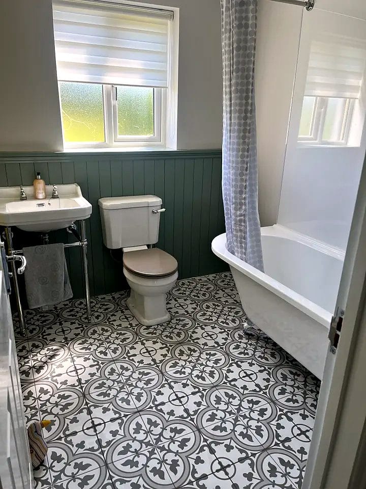 Bathroom with green tongue-and-groove panelling, roll-top bath and patterned floor tiles