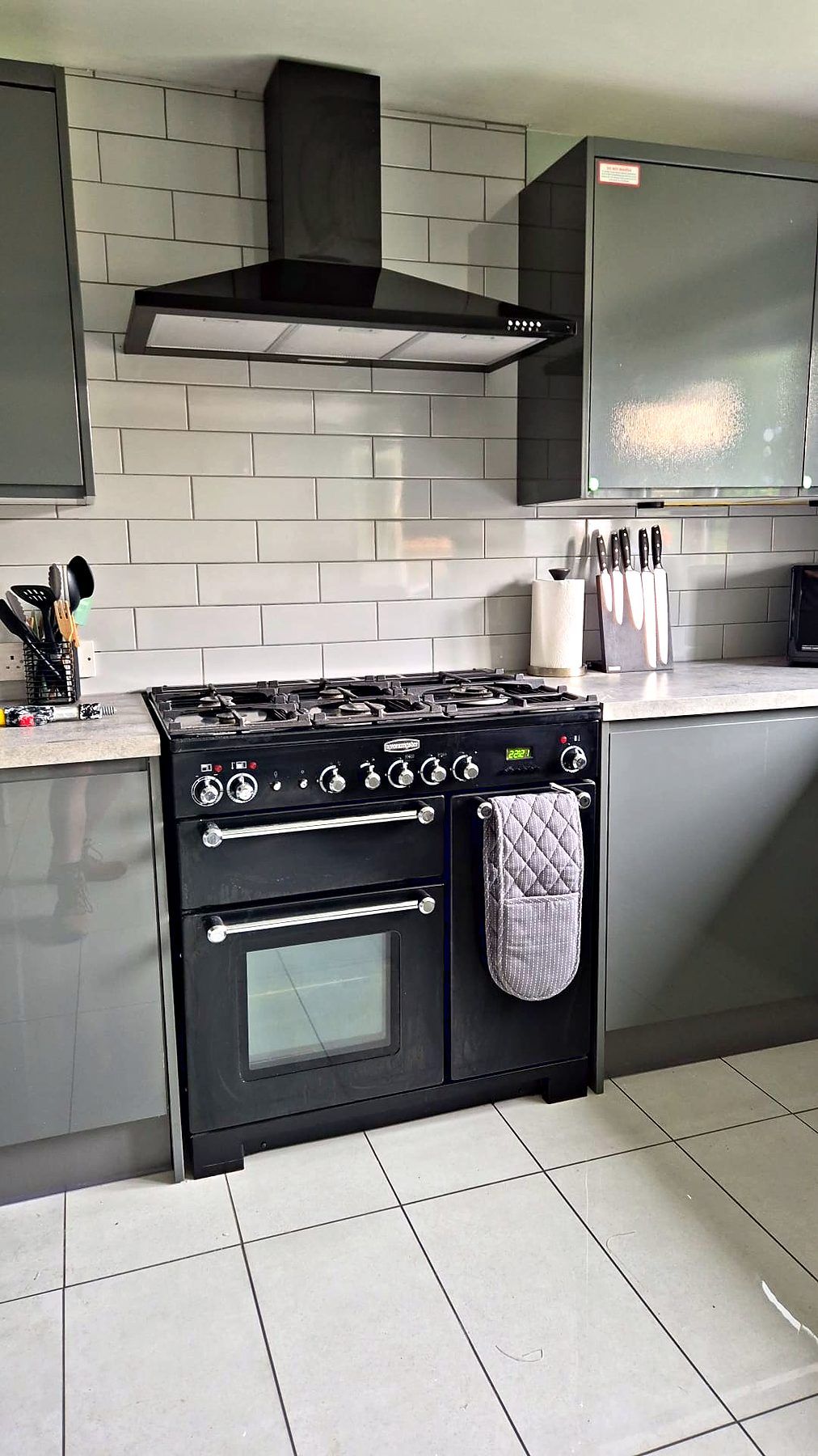 Black range cooker beneath a chimney hood with white metro tiling and graphite units