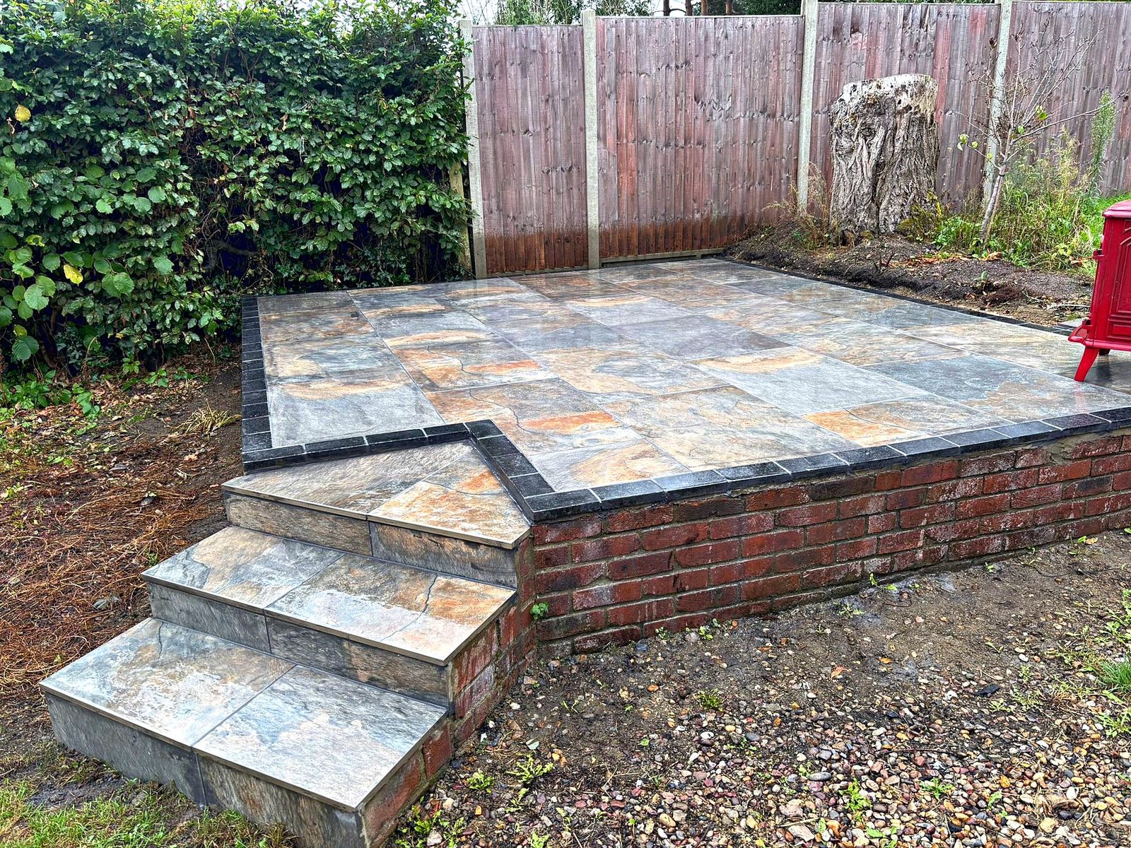 Close view of a porcelain-tiled patio with dark edging on a red brick plinth