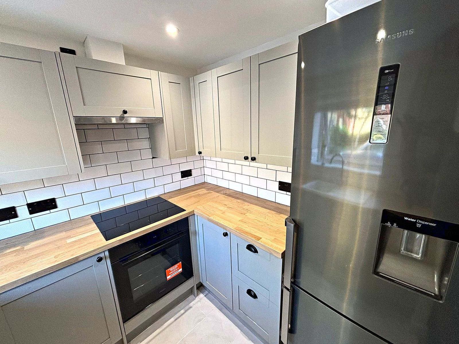 Sage shaker kitchen corner with induction hob, oak worktops and a freestanding fridge freezer