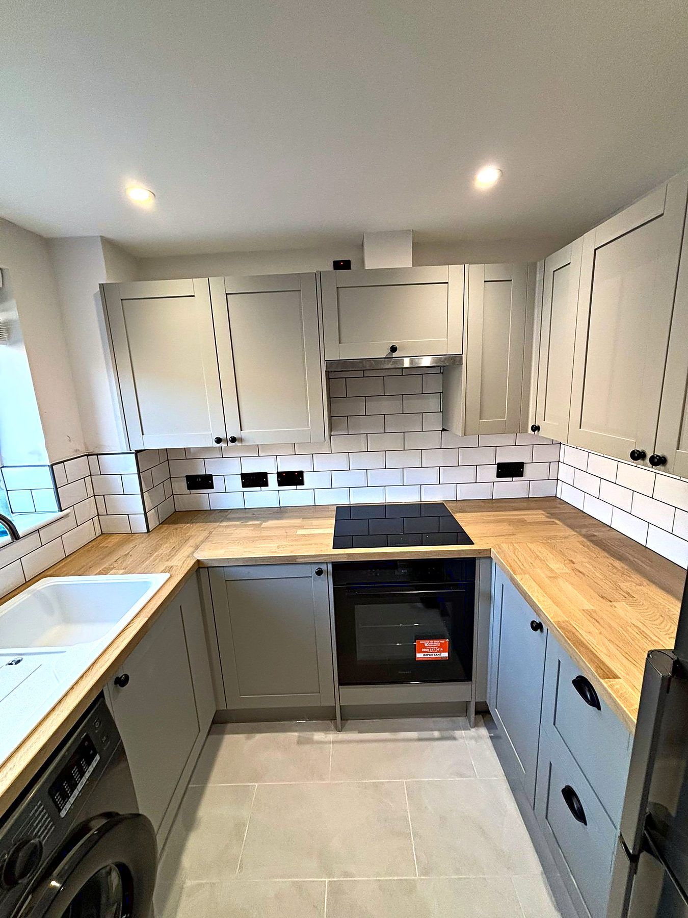 Sage shaker kitchen with solid oak worktops, white metro tiling and black sockets