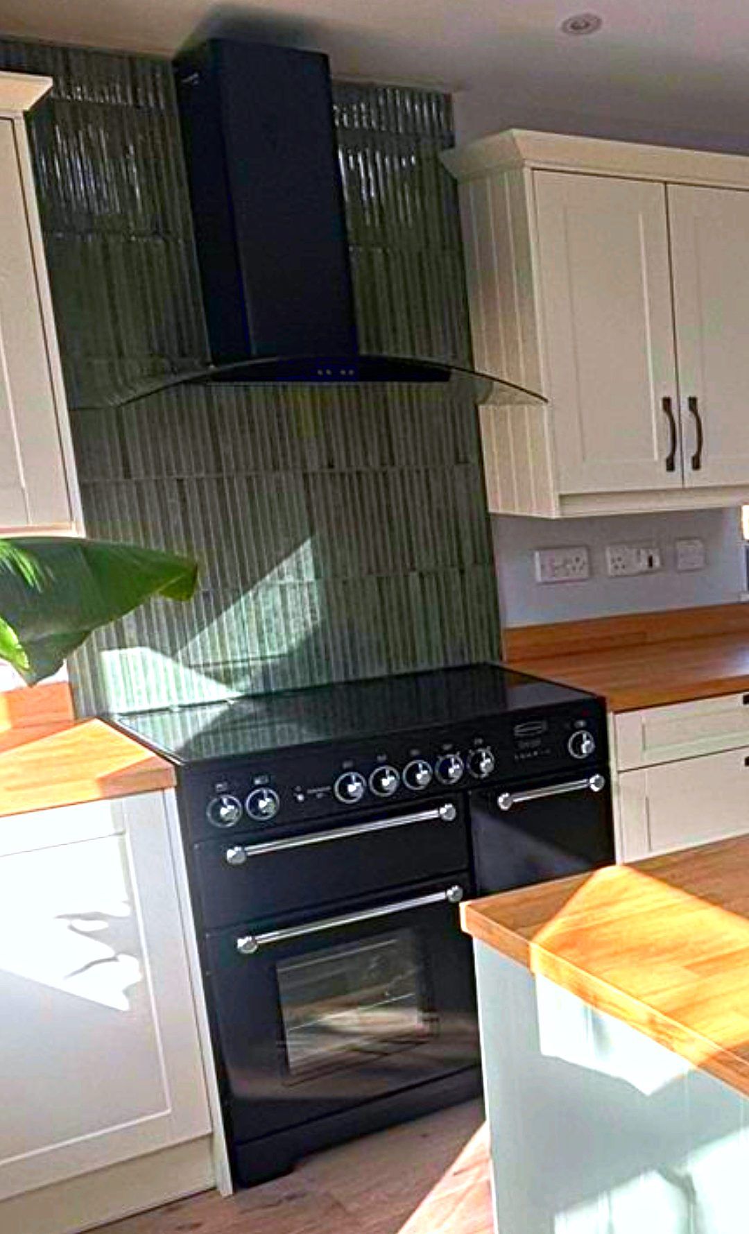 Kitchen with green glazed splashback tiles, black range cooker, cream cabinetry and oak worktops
