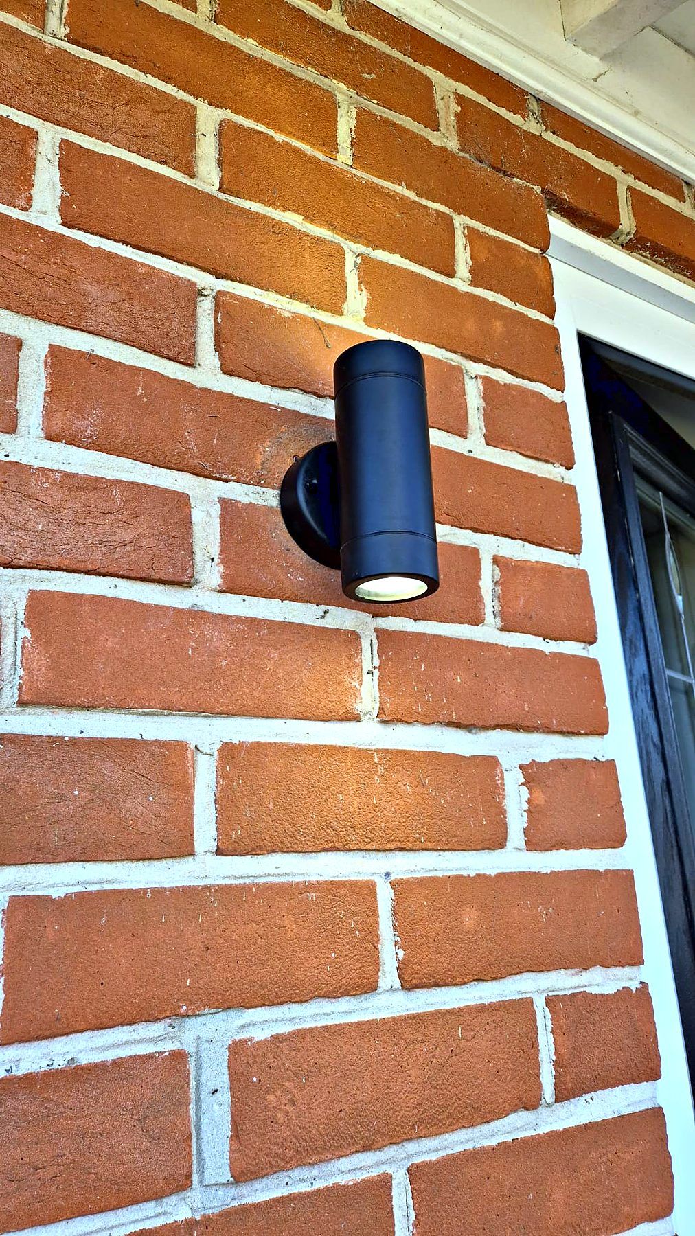 Black exterior up-and-down wall light fitted to red brickwork beside a door