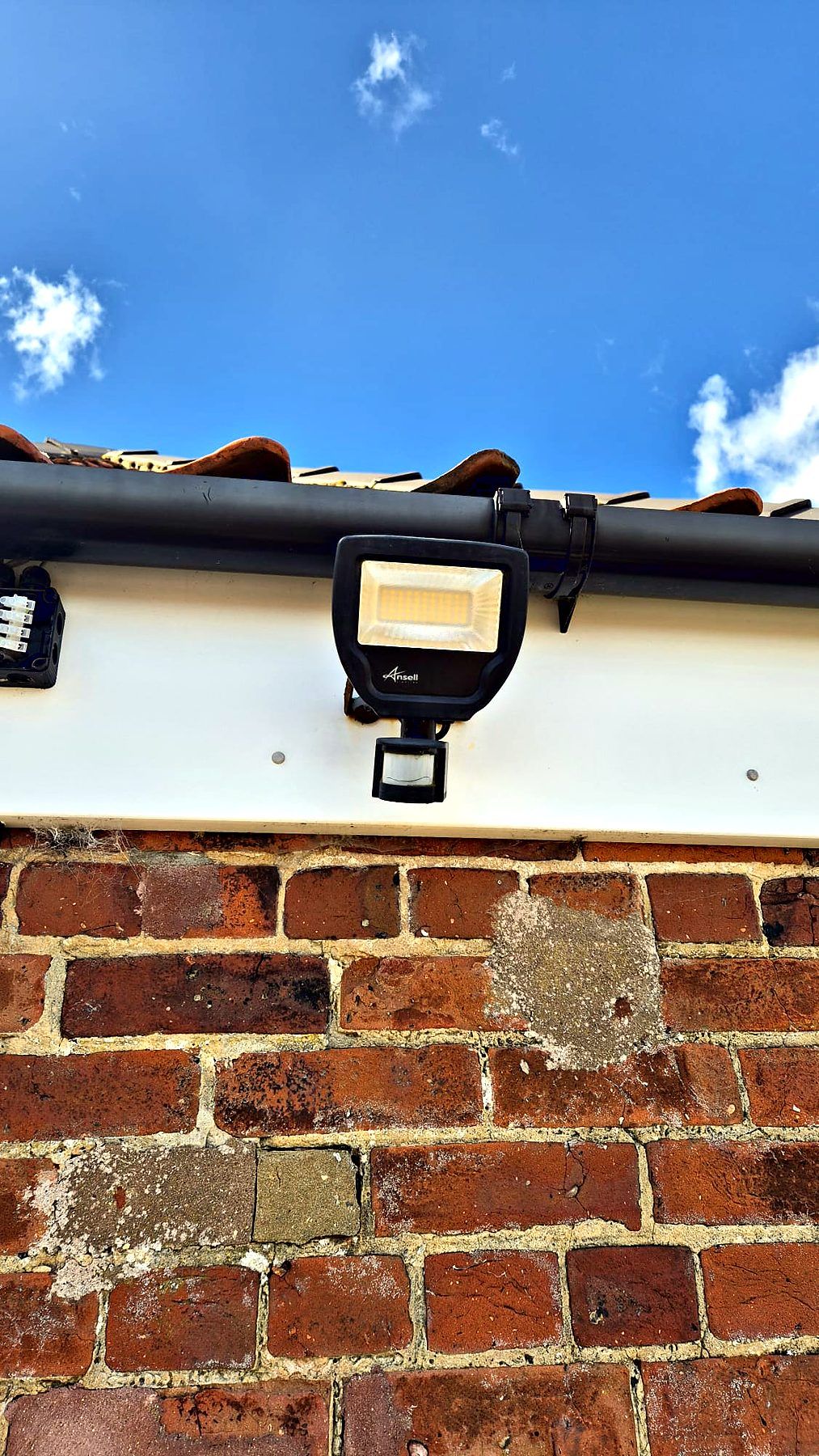 LED floodlight with PIR sensor fitted beneath the eaves of a brick building