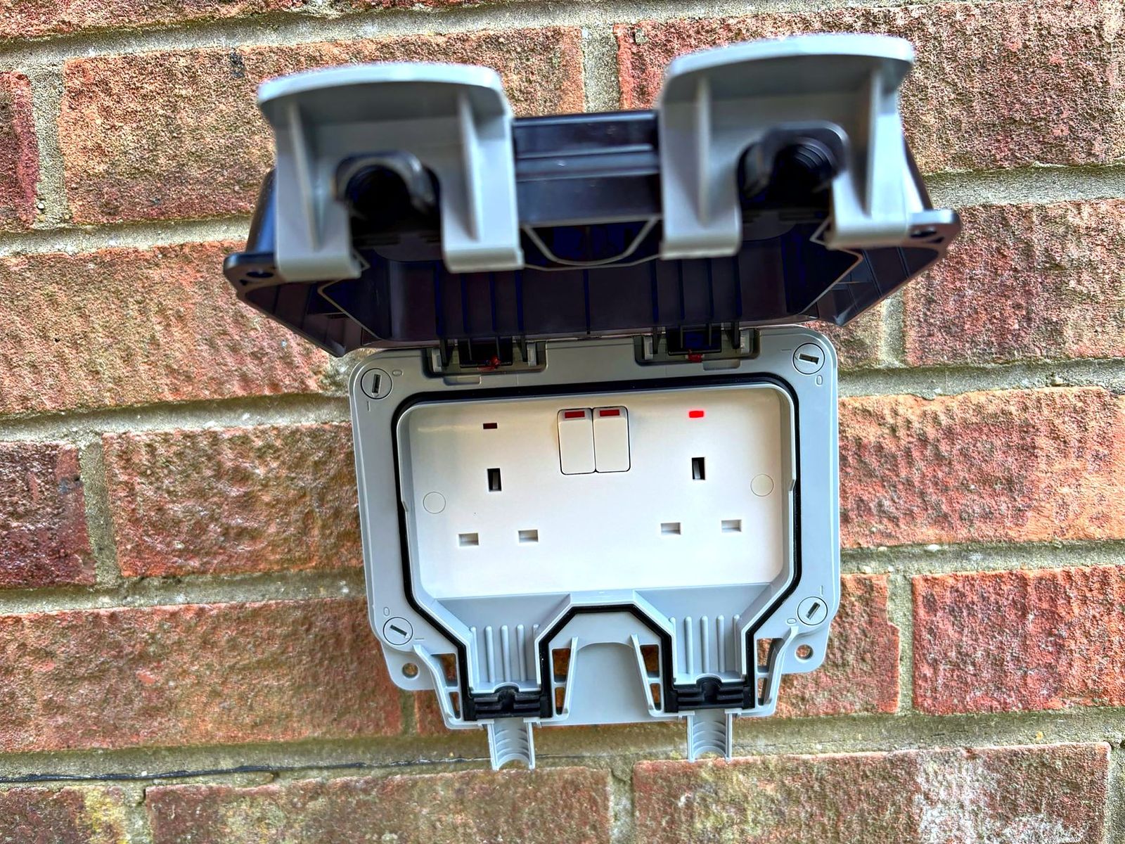 Weatherproof double outdoor socket fitted to a brick wall, lid open