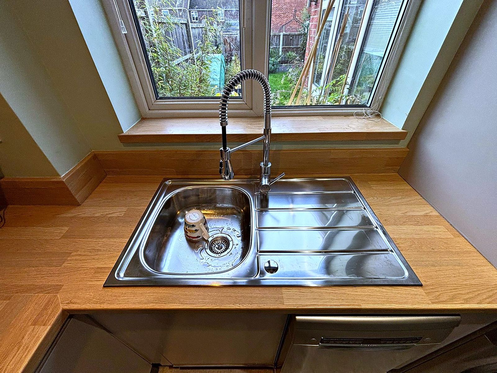 Stainless steel inset sink and spring mixer tap in a solid oak worktop beneath a window
