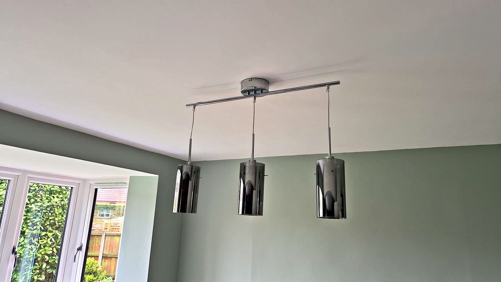 Triple chrome pendant light bar installed in a sage green room
