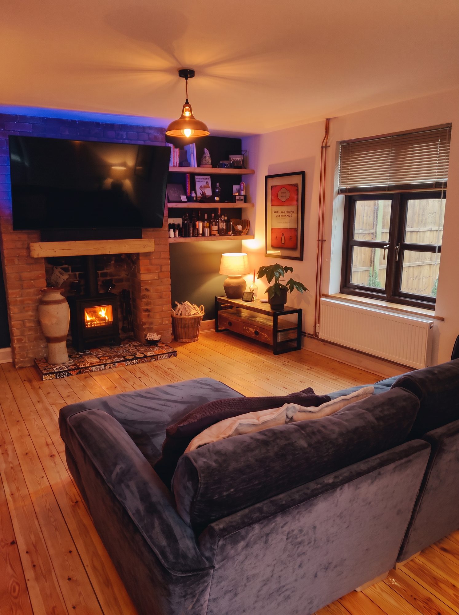 Living room with warm ceiling lighting, oak alcove shelving, a lit fire and restored timber floor